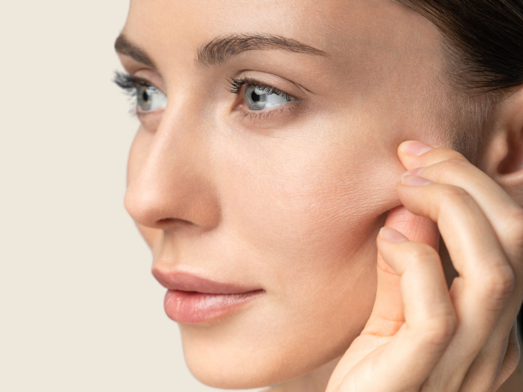 Healthy beautiful Woman, side left face pinching her cheeks with beige background.