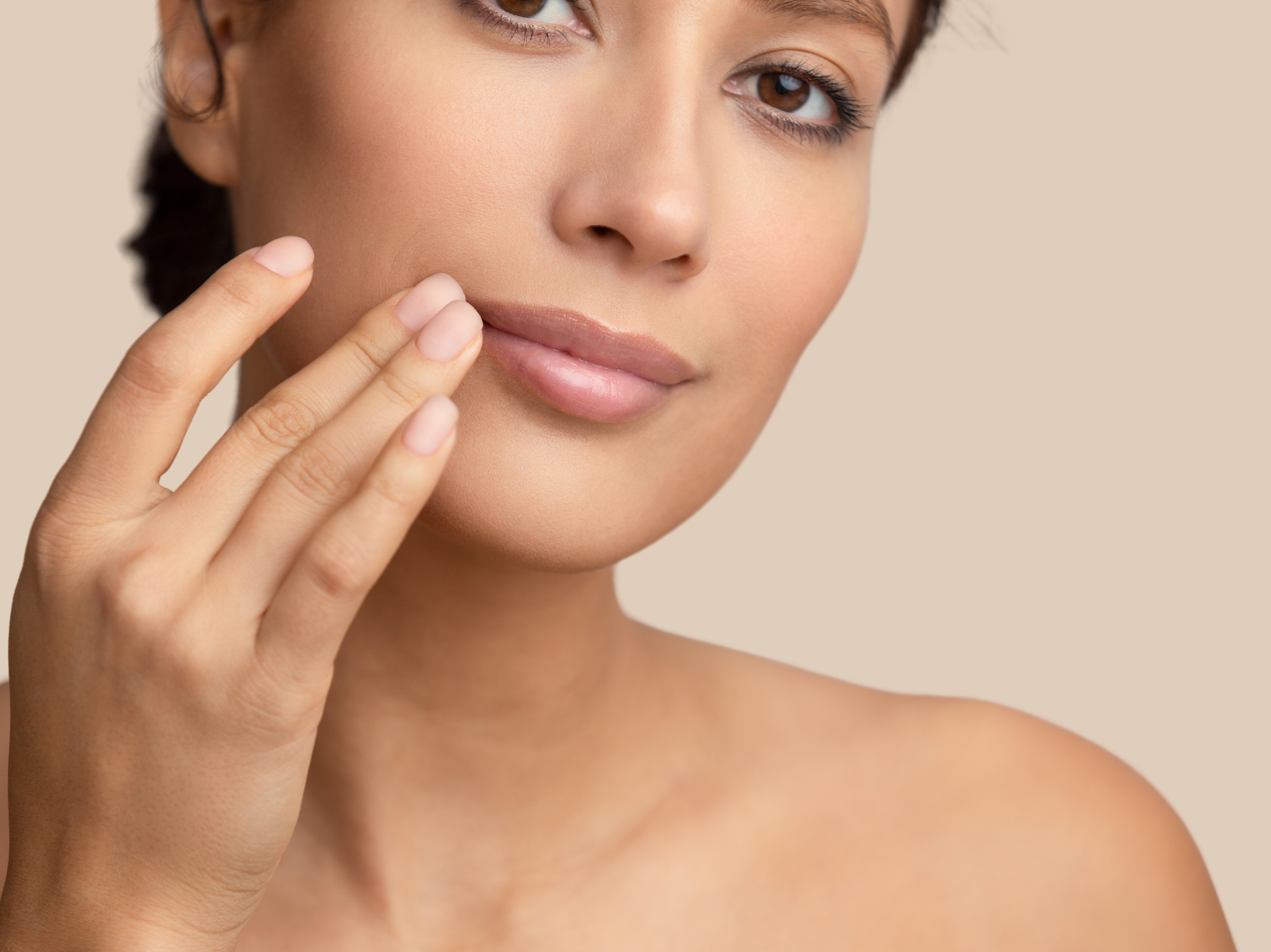 Non invasive Image Healthy woman great skin touching side of mouth, beige background.